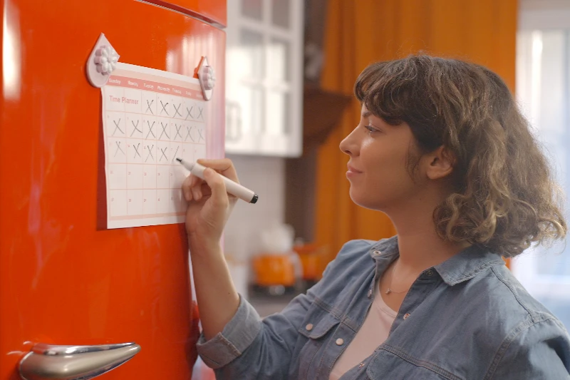 Woman marking off her calendar on a fridge