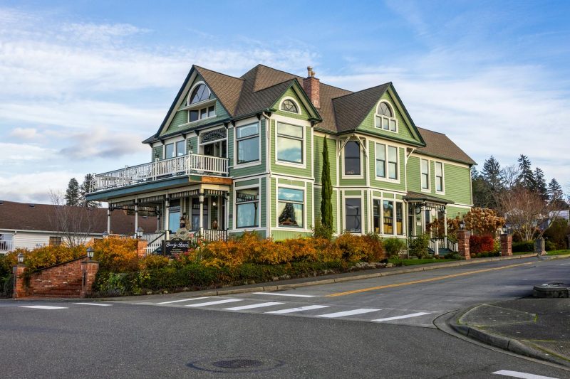 A charming green Victorian house with intricate architectural details situated on a corner street.