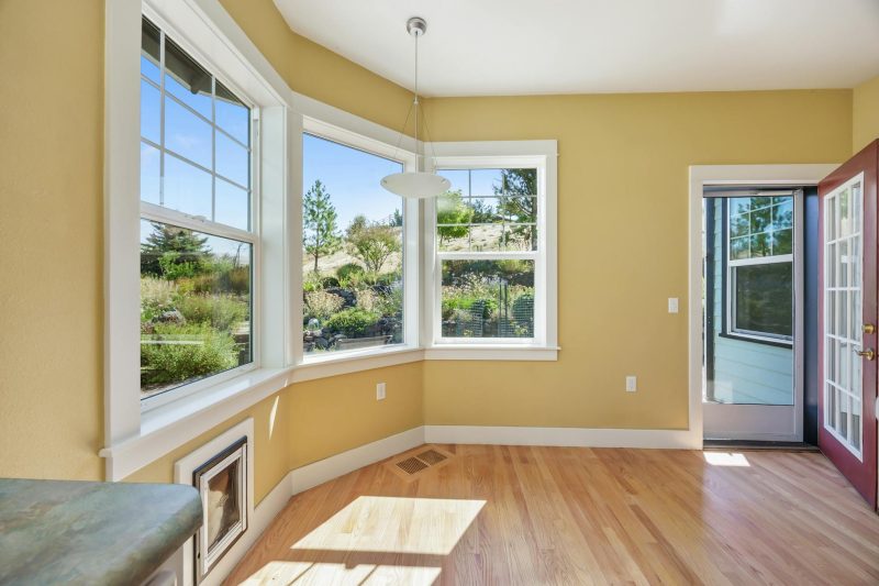Spacious sunlit room with wooden floors and large windows displaying views of a tranquil garden.