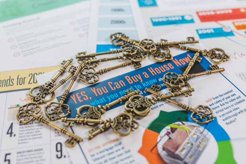 A collection of vintage keys scattered atop a real estate brochure promoting house buying.